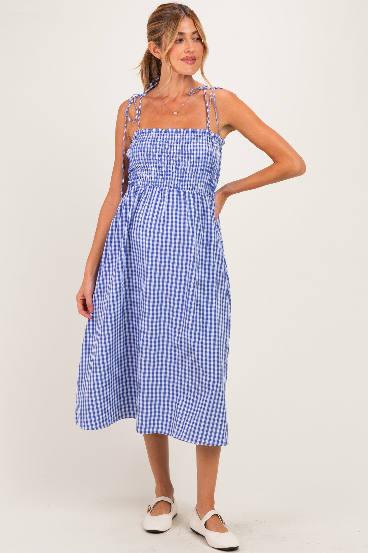 woman wearing a blue and white gingham maternity dress with adjustable straps and a visible baby bump