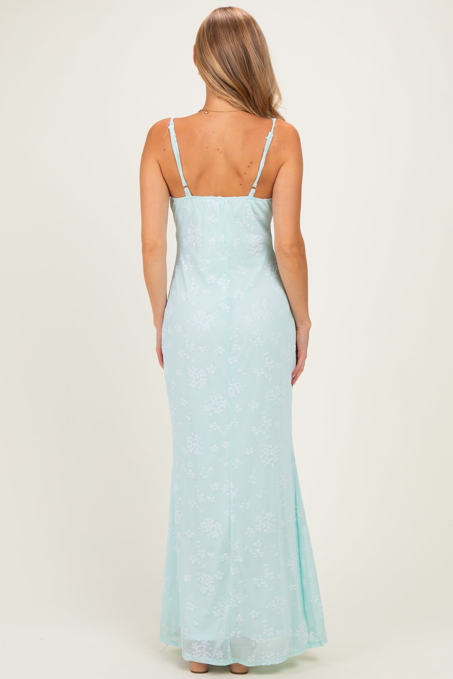 woman wearing a light mint green floral maxi dress with thin straps, shown from the back