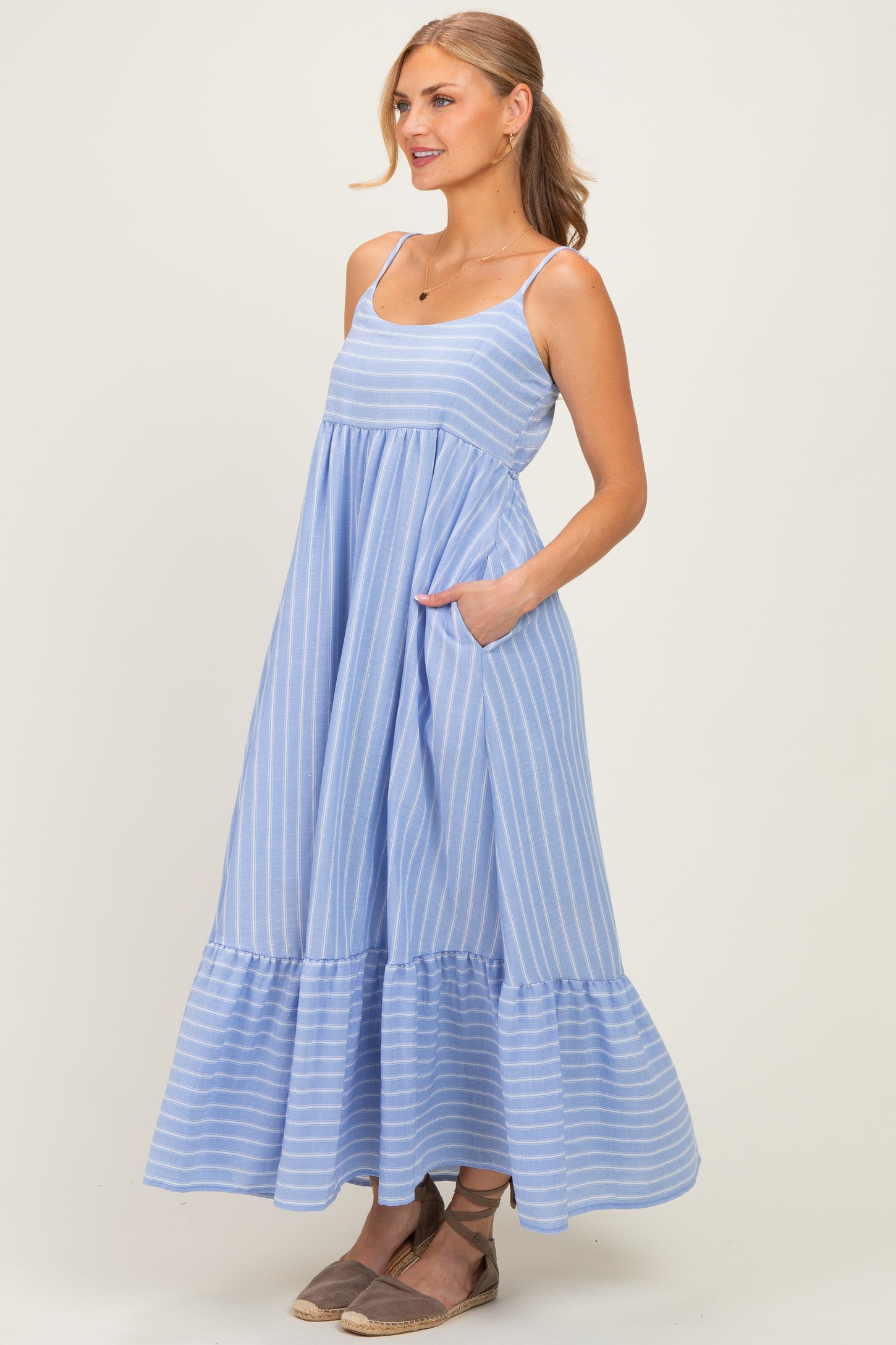 woman wearing a light blue striped maxi dress with a tiered ruffle hem and pockets, styled with espadrille shoes