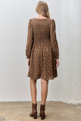 woman wearing a brown floral smocked mini dress with long sleeves and a slight flare at the hem