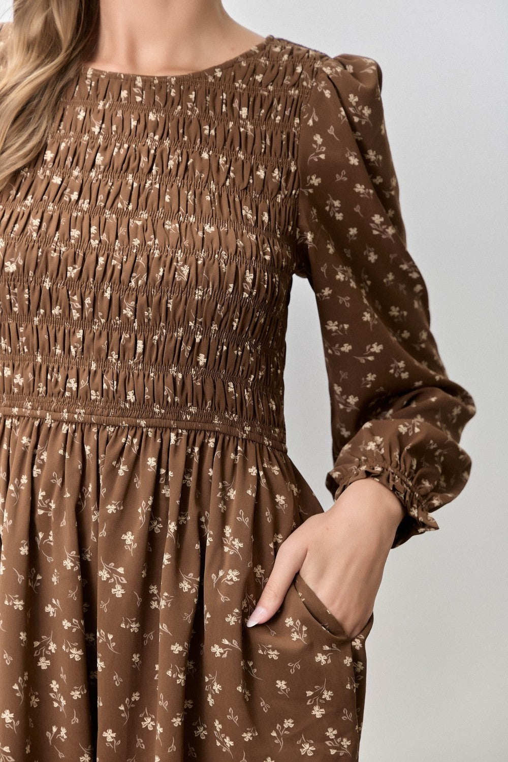 woman wearing a brown floral smocked dress with long sleeves and pockets