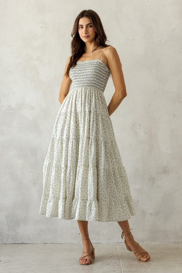 woman wearing a white floral maxi dress with thin straps and a smocked bodice, standing against a neutral backdrop