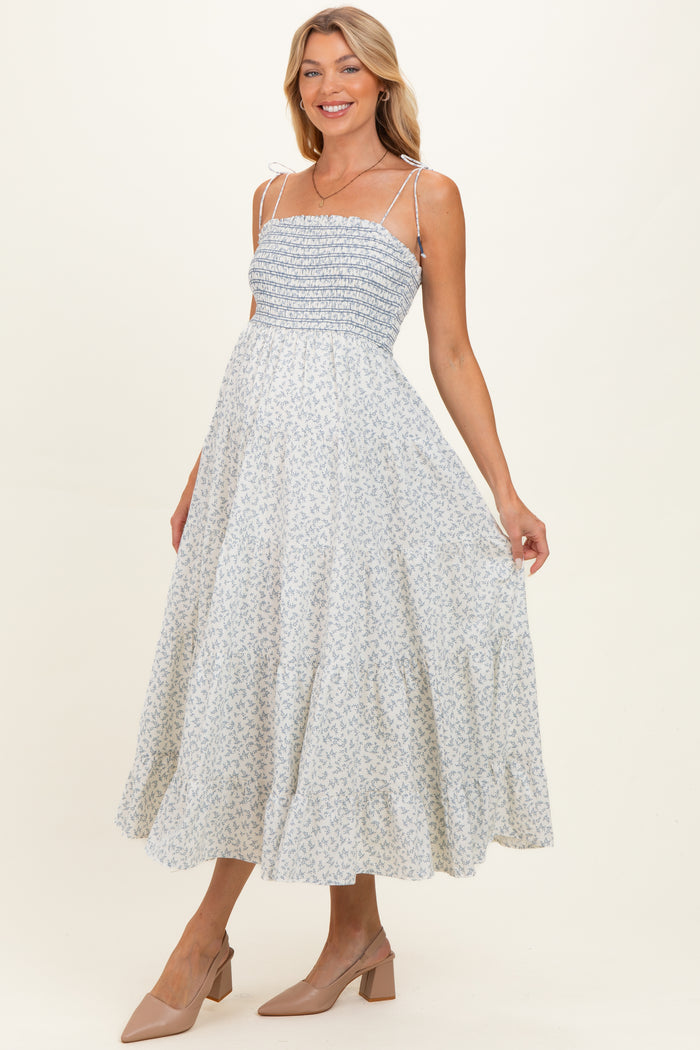 woman wearing a light blue floral maternity dress with smocked bodice and adjustable straps, holding her baby bump