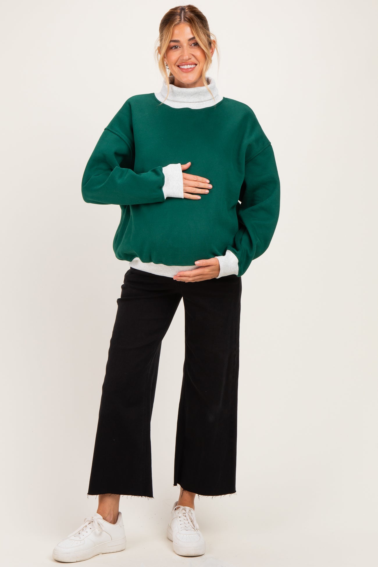 woman wearing a green oversized maternity sweatshirt with white sleeves and a visible baby bump