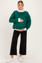 woman wearing a green oversized maternity sweatshirt with white sleeves and a visible baby bump