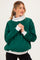 woman wearing a green maternity sweatshirt with a light gray collar and cuffs, standing with hands clasped in front