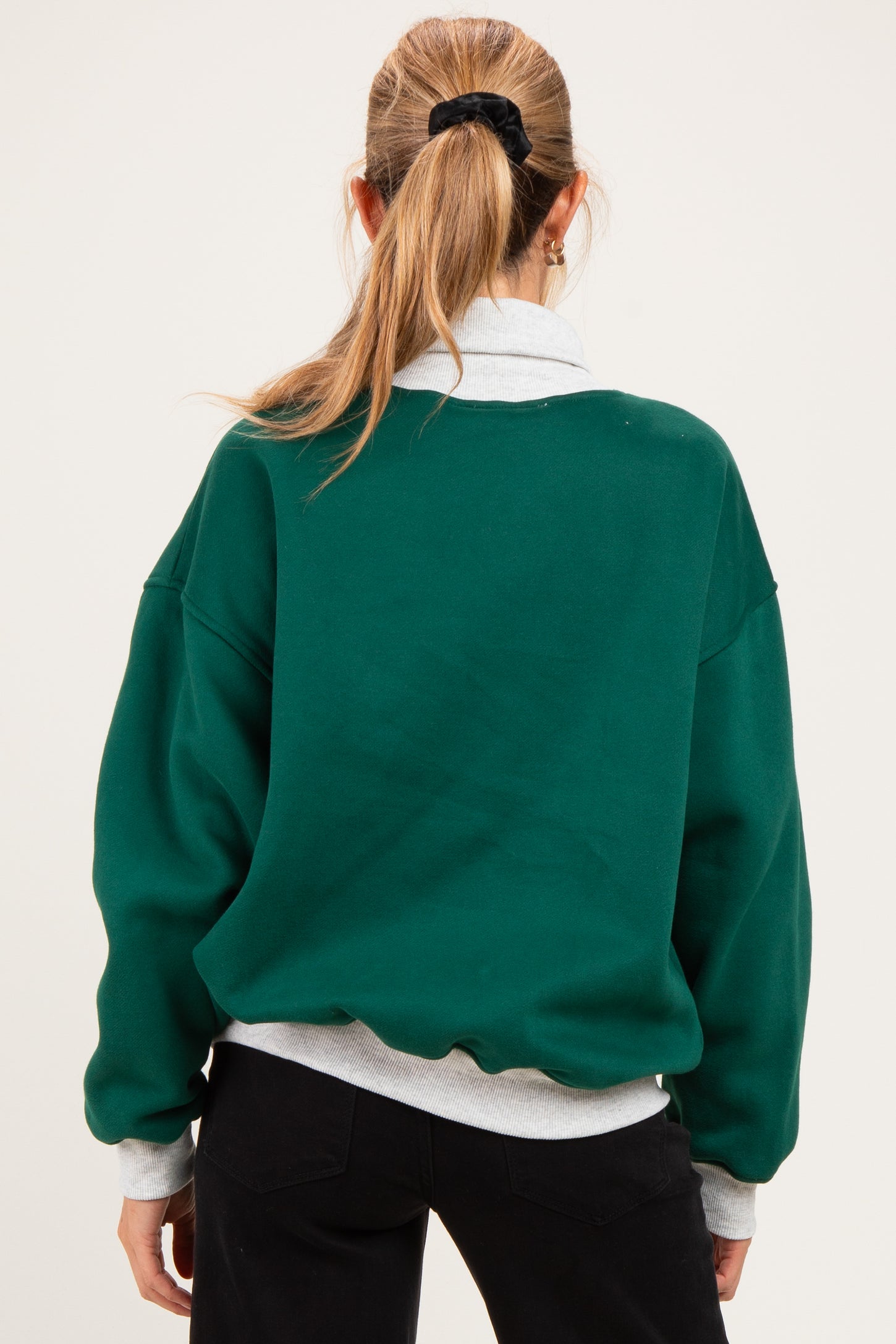 woman wearing a green oversized maternity sweatshirt with a light gray collar styled backward, showcasing a relaxed fit