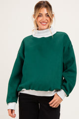 woman wearing a dark green maternity sweatshirt with a light gray turtleneck underneath and a relaxed fit