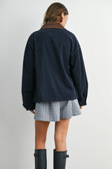 woman wearing a navy blue corduroy oversized jacket with brown collar and checkered skirt, seen from the back