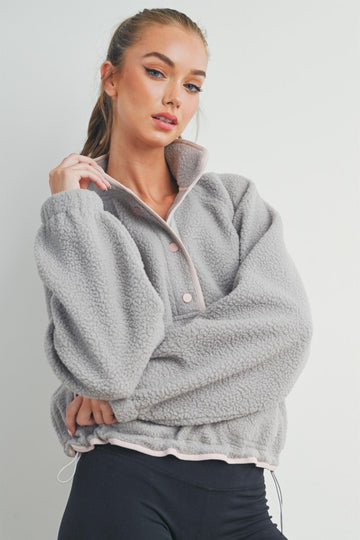 woman wearing a gray fleece pullover jacket with a zip collar and pink detailing, posing with one hand on her hip