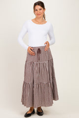 woman wearing a white long sleeve maternity top and a brown gingham tiered maternity skirt, holding her baby bump