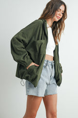 woman wearing an oversized olive green corduroy jacket with front pockets and a white crop top with denim shorts