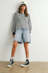 woman wearing a gray and white striped long sleeve polo shirt with denim bermuda shorts and black sneakers