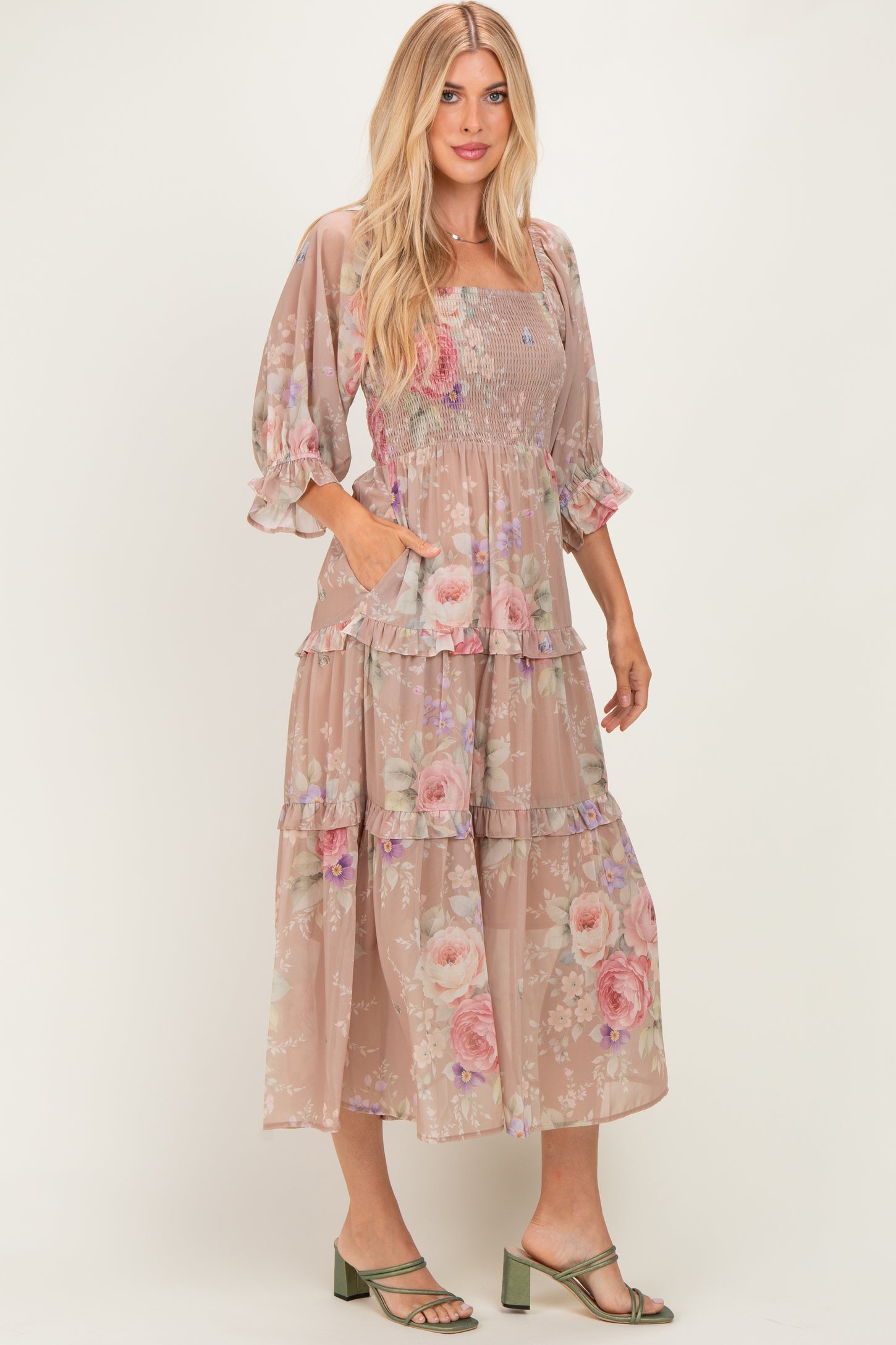 woman wearing a beige floral tiered maxi dress with puff sleeves and pockets, standing in strappy green heels