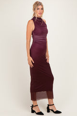 woman wearing a burgundy sleeveless midi dress with ruching details and a sheer lower hem, styled with black ankle strap heels