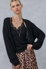 woman wearing a black cable knit cardigan over a black lace camisole and pink leopard print skirt