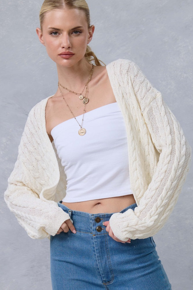 woman wearing a cream cable-knit cardigan over a white tube top and high-waisted denim jeans