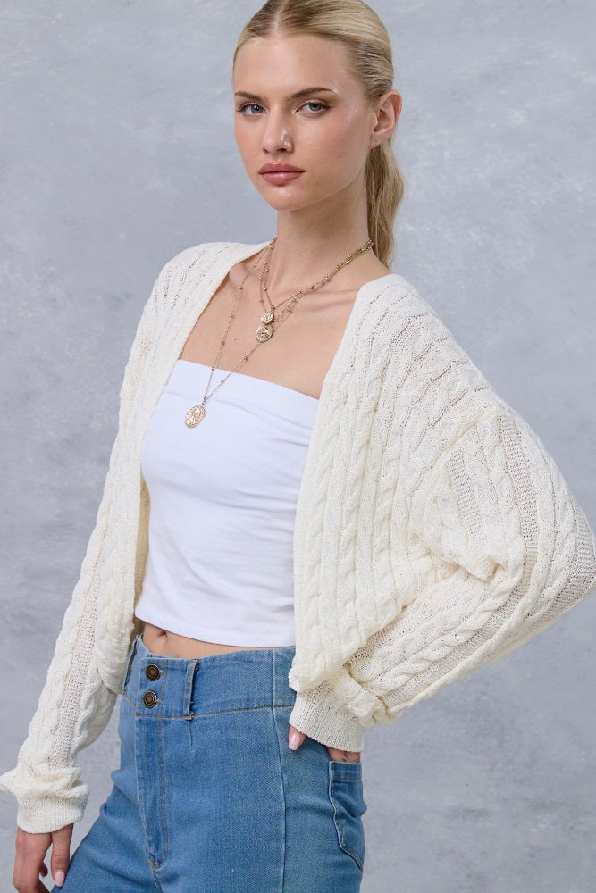 woman wearing a cream cable knit cardigan over a white strapless top and high-waisted jeans, styled with layered necklaces