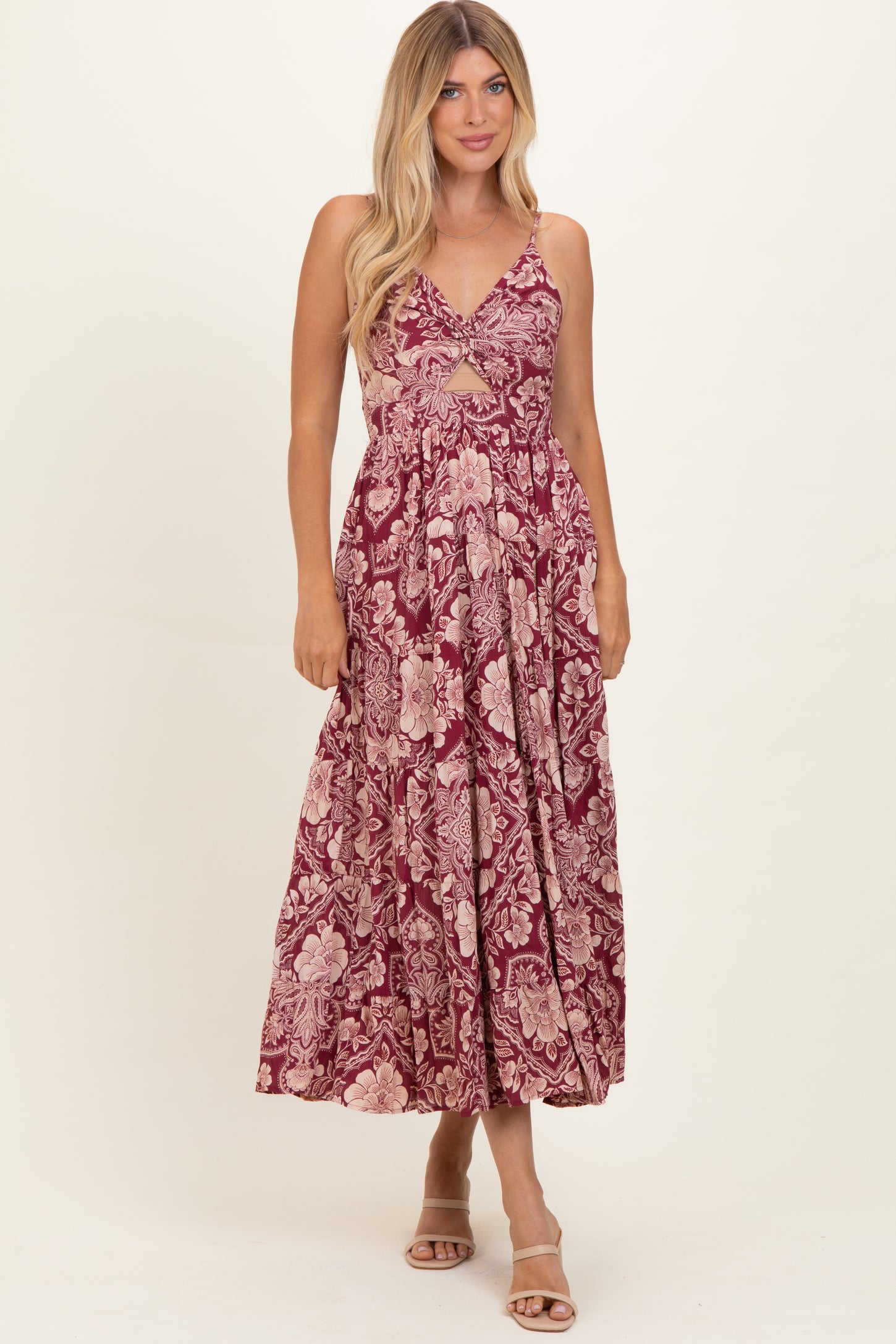 woman wearing a burgundy maxi dress with a floral print and cut-out details, standing against a neutral background