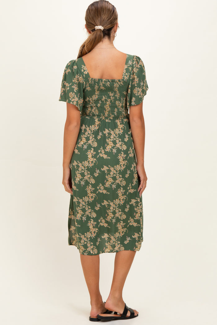 woman wearing a green floral maternity dress with short sleeves, showing the back view and gathered detailing
