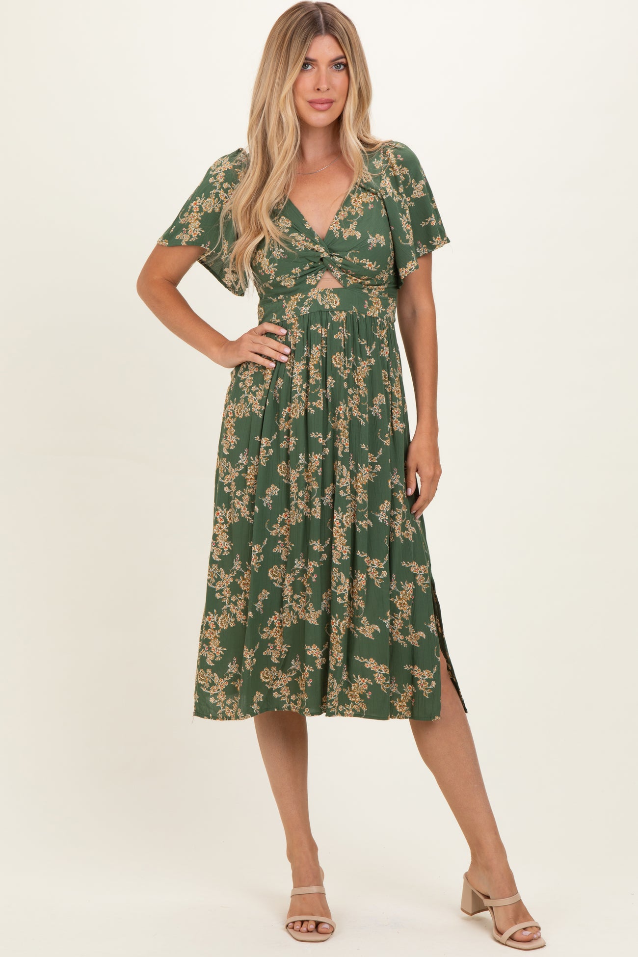 woman wearing a green floral print midi dress with a twist front and short sleeves, standing in a neutral background