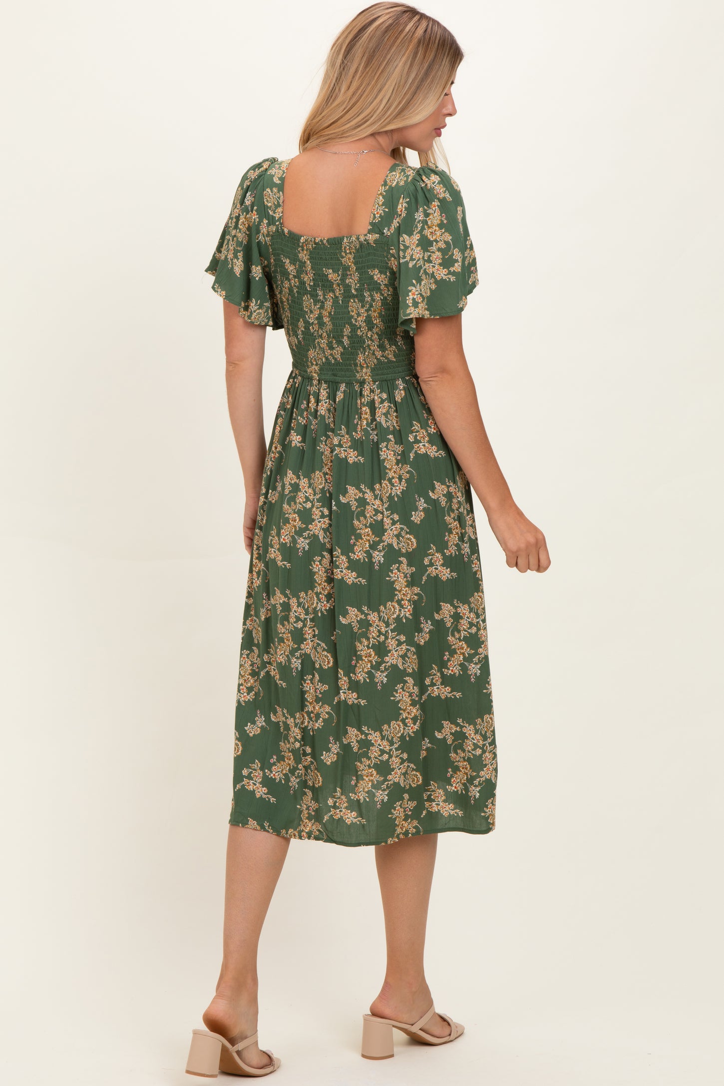 woman wearing a green floral midi dress with short flutter sleeves and a smocked back, shown from the back