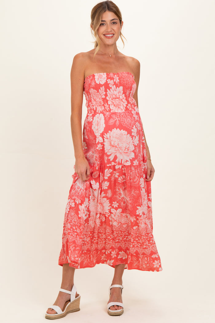 woman wearing a strapless coral maternity dress with floral print and a flowing maxi length, showing her baby bump