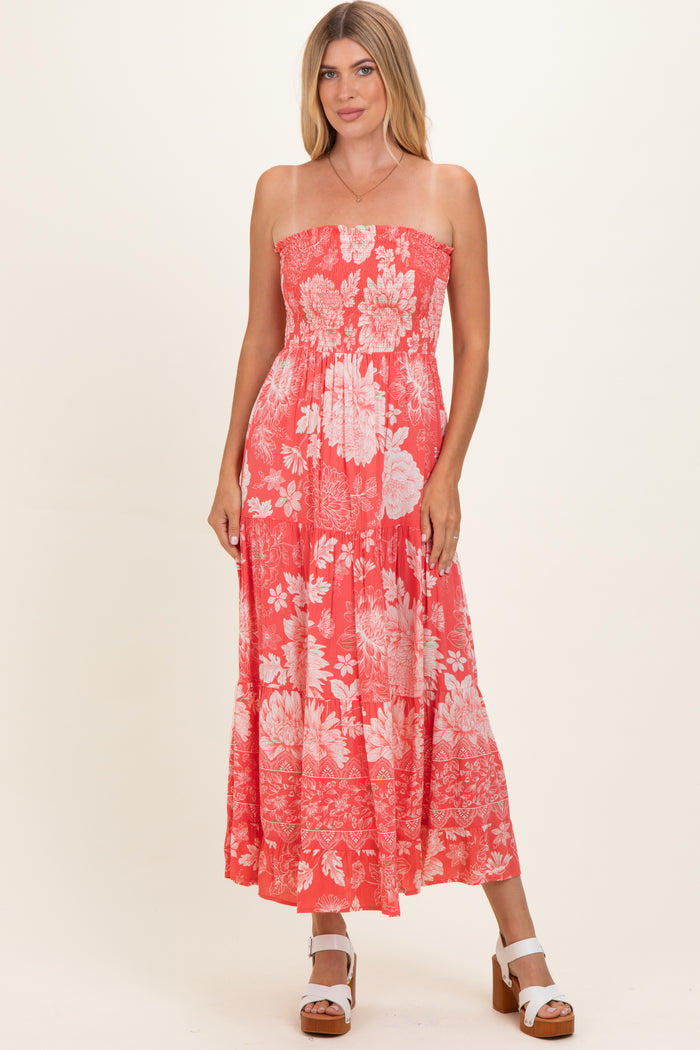 woman wearing a coral strapless maxi dress with a floral pattern and a fitted bodice, standing in a neutral background