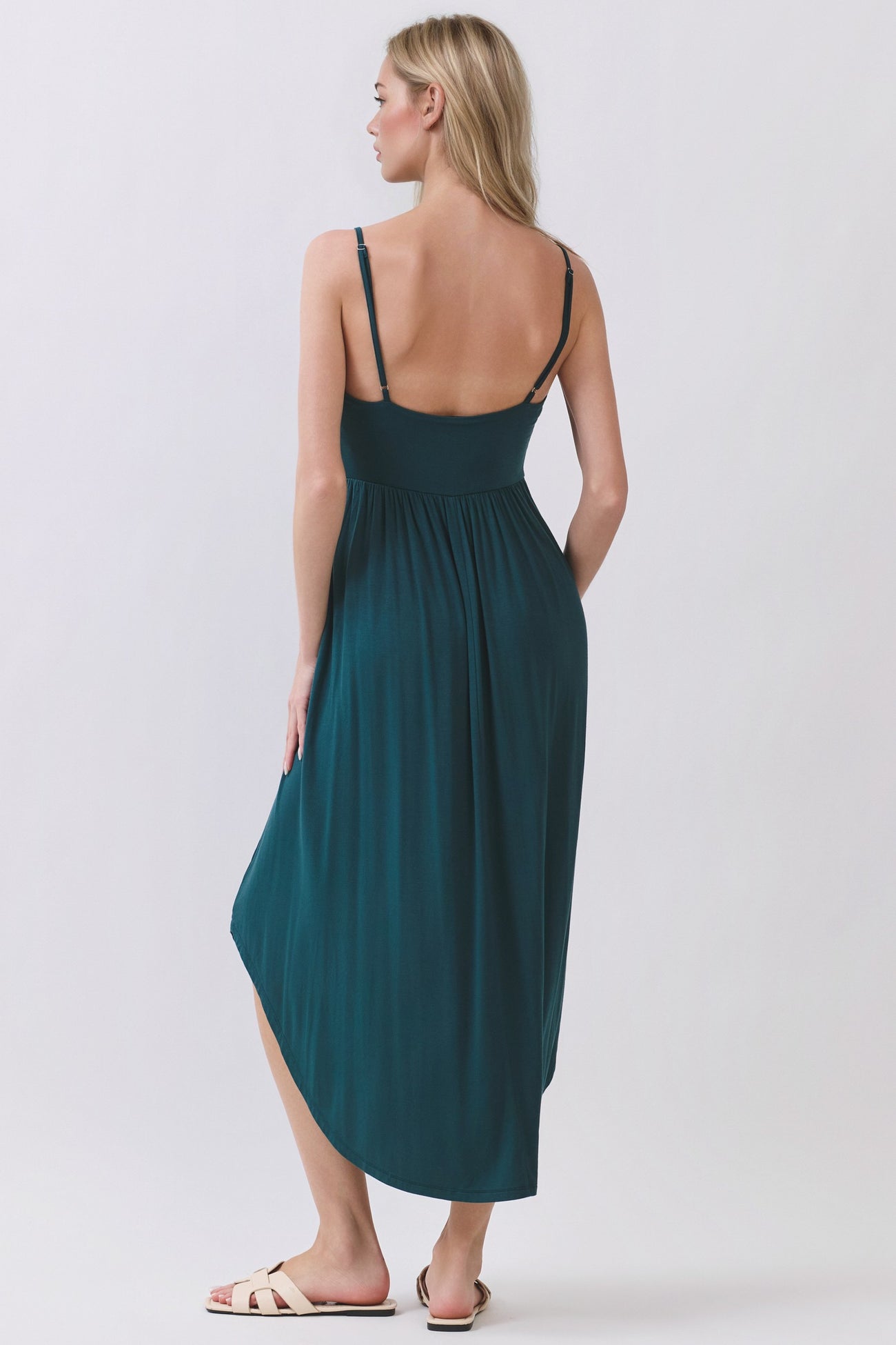 woman wearing a teal maxi dress with adjustable straps and a high-low hem, viewed from the back