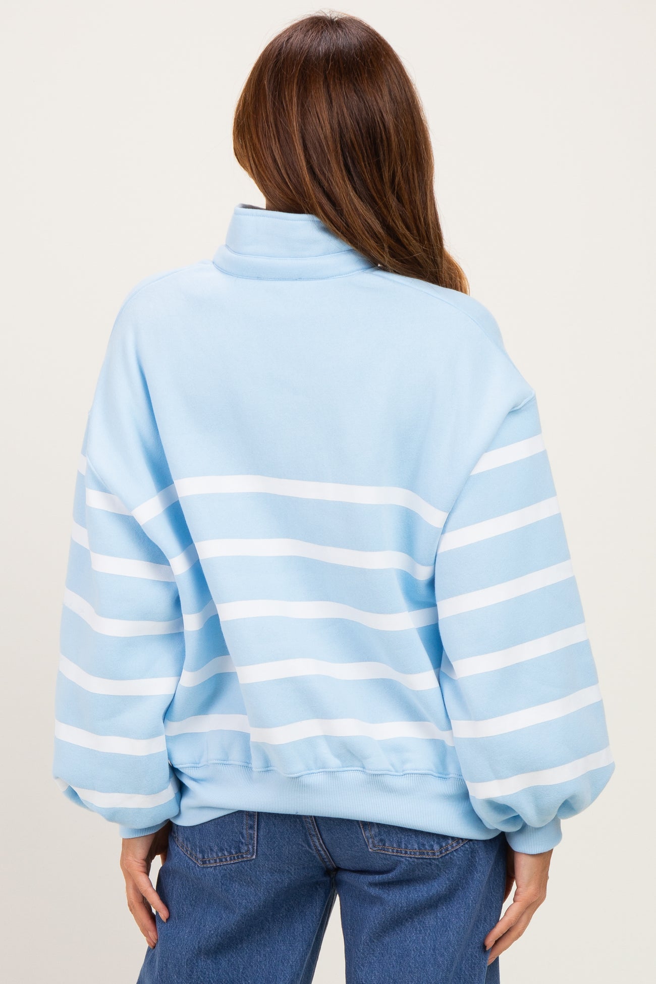 woman wearing a light blue oversized pullover sweatshirt with white stripes on the back and side detail