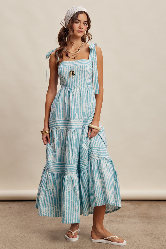 woman wearing a light blue striped sundress with tie straps and tiered skirt, accessorized with a white headband and jewelry