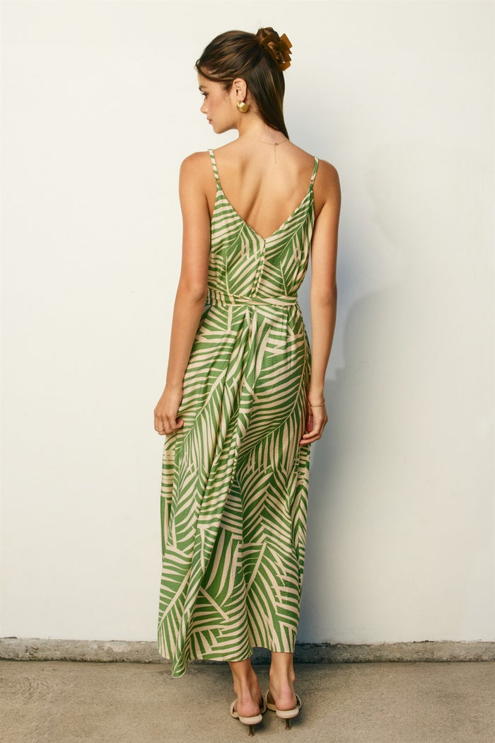 woman wearing a green palm leaf print maxi dress with a back tie detail and spaghetti straps
