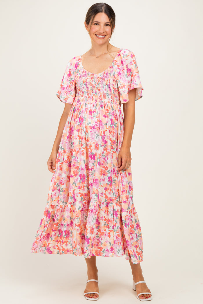 woman wearing a pink floral maternity maxi dress with short flutter sleeves and a smocked bodice