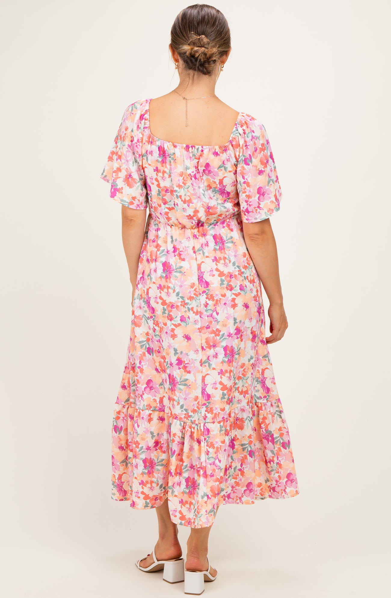 woman wearing a floral pink maternity dress with flutter sleeves and a tiered hem, showing a baby bump from the back