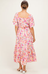 woman wearing a floral pink maternity dress with flutter sleeves and a tiered hem, showing a baby bump from the back