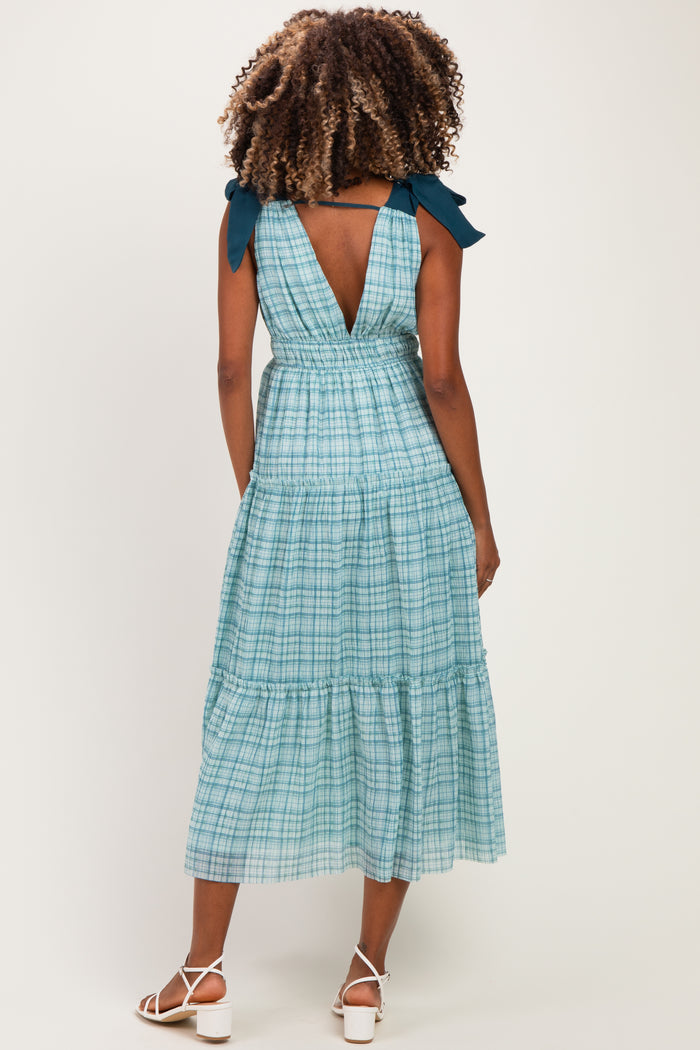 woman wearing a green and blue plaid maternity dress with a back tie detail and tiered skirt.