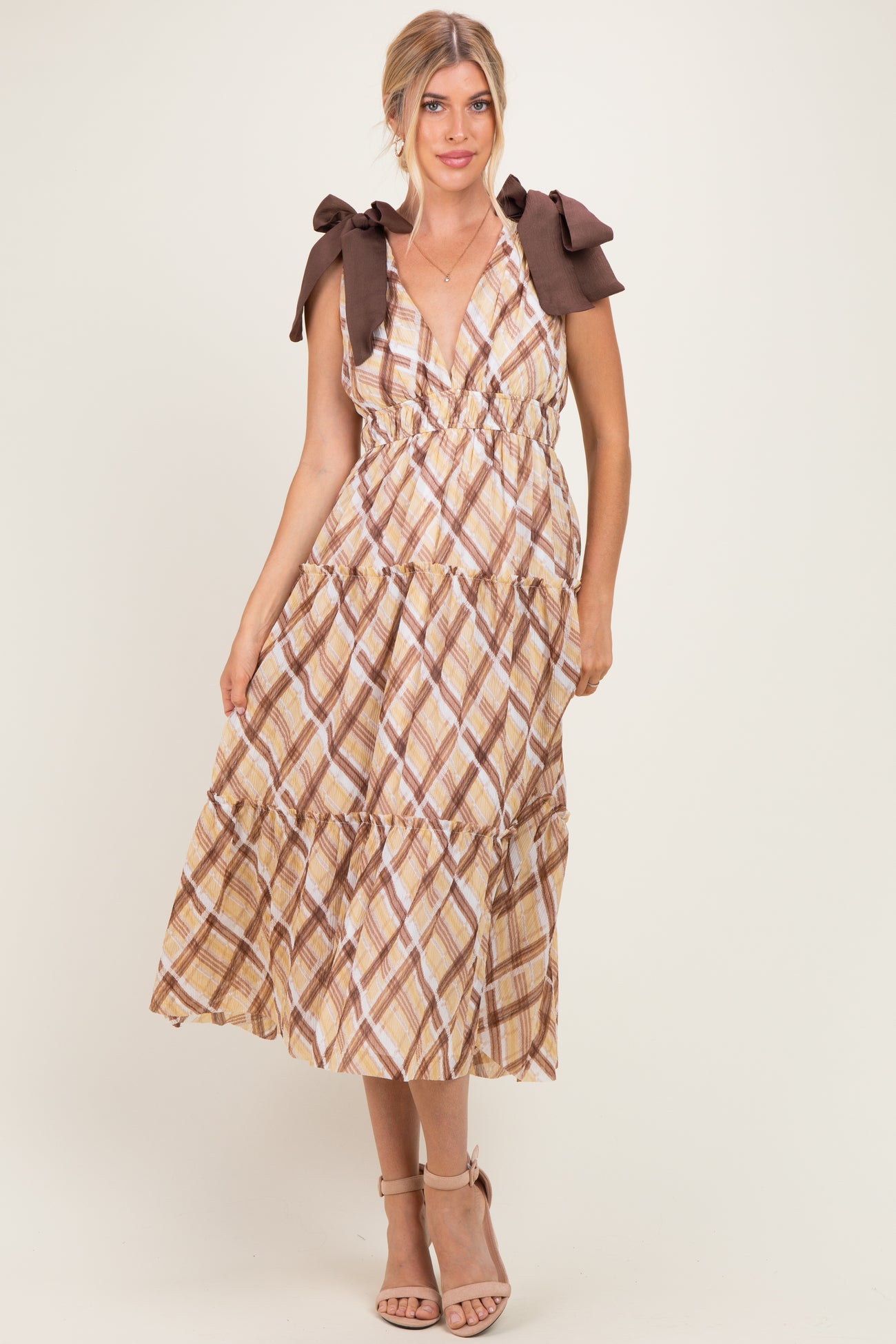 woman wearing a beige and brown plaid maxi dress with tie shoulder straps and a tiered skirt