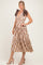 woman wearing a brown and beige plaid midi dress with a tiered skirt and bow tie straps, standing in a neutral background