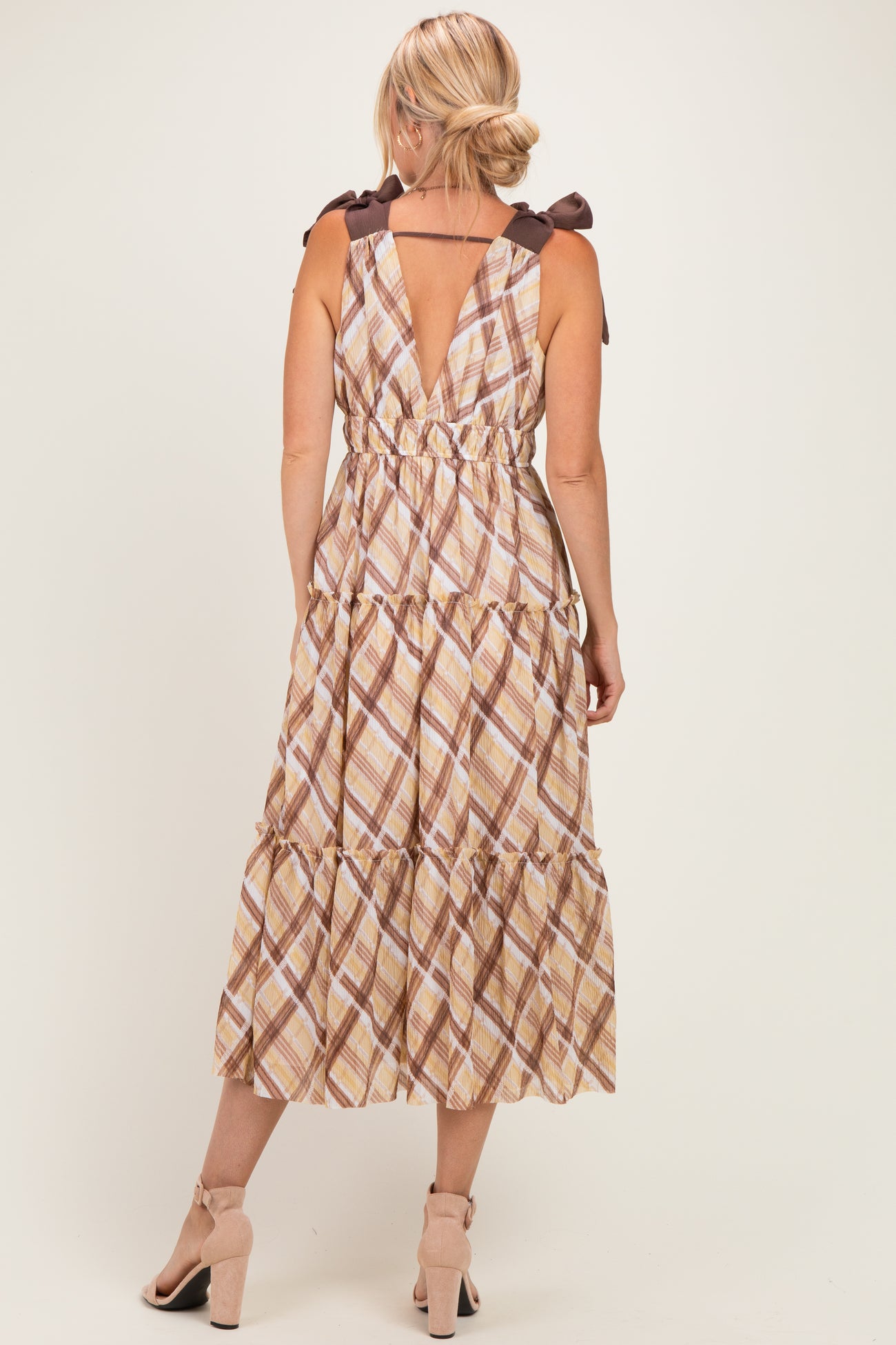 woman wearing a brown and cream plaid maxi dress with tie shoulder straps and a tiered skirt, shown from the back