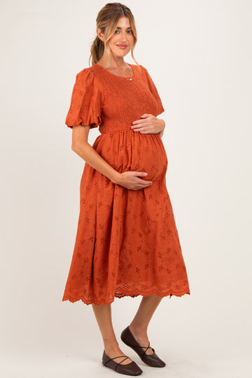 woman wearing an orange maternity dress with puff sleeves and a smocked bodice, holding her baby bump
