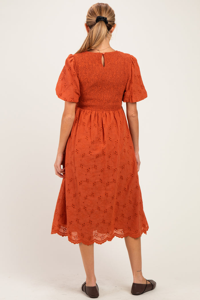 woman wearing an orange maternity dress with short puff sleeves and embroidery details, showing the back view