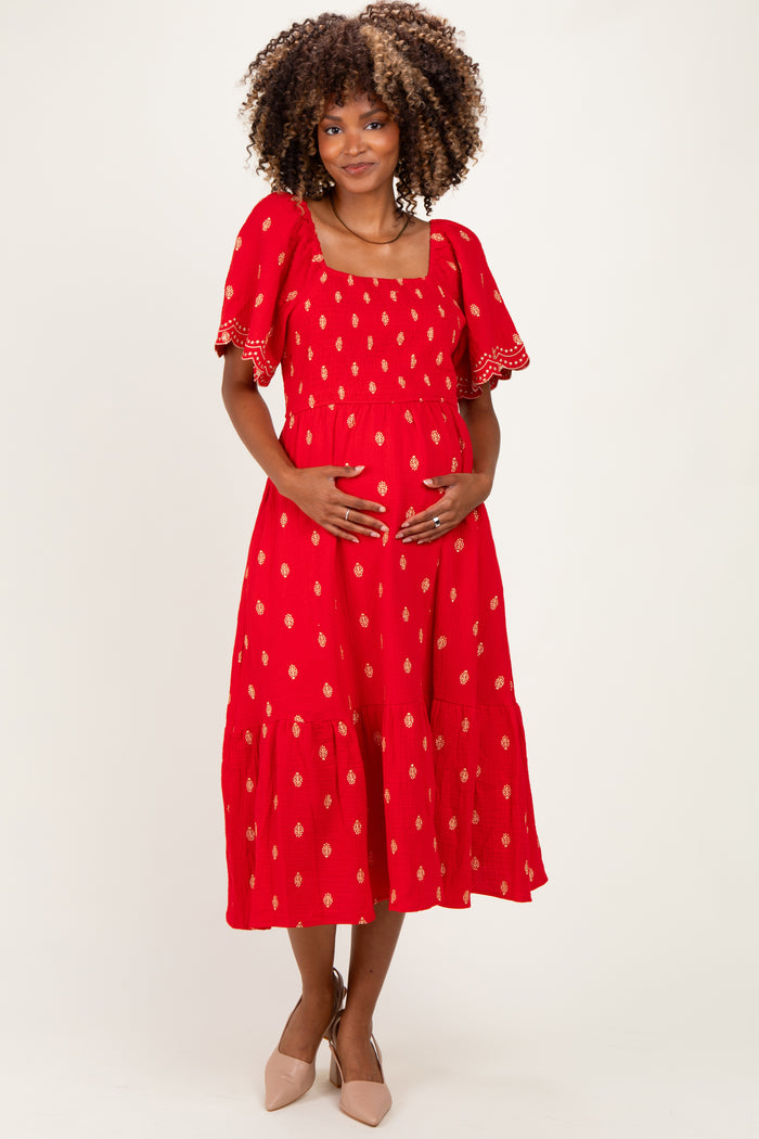 woman wearing a red patterned maternity dress with puff sleeves and holding her baby bump