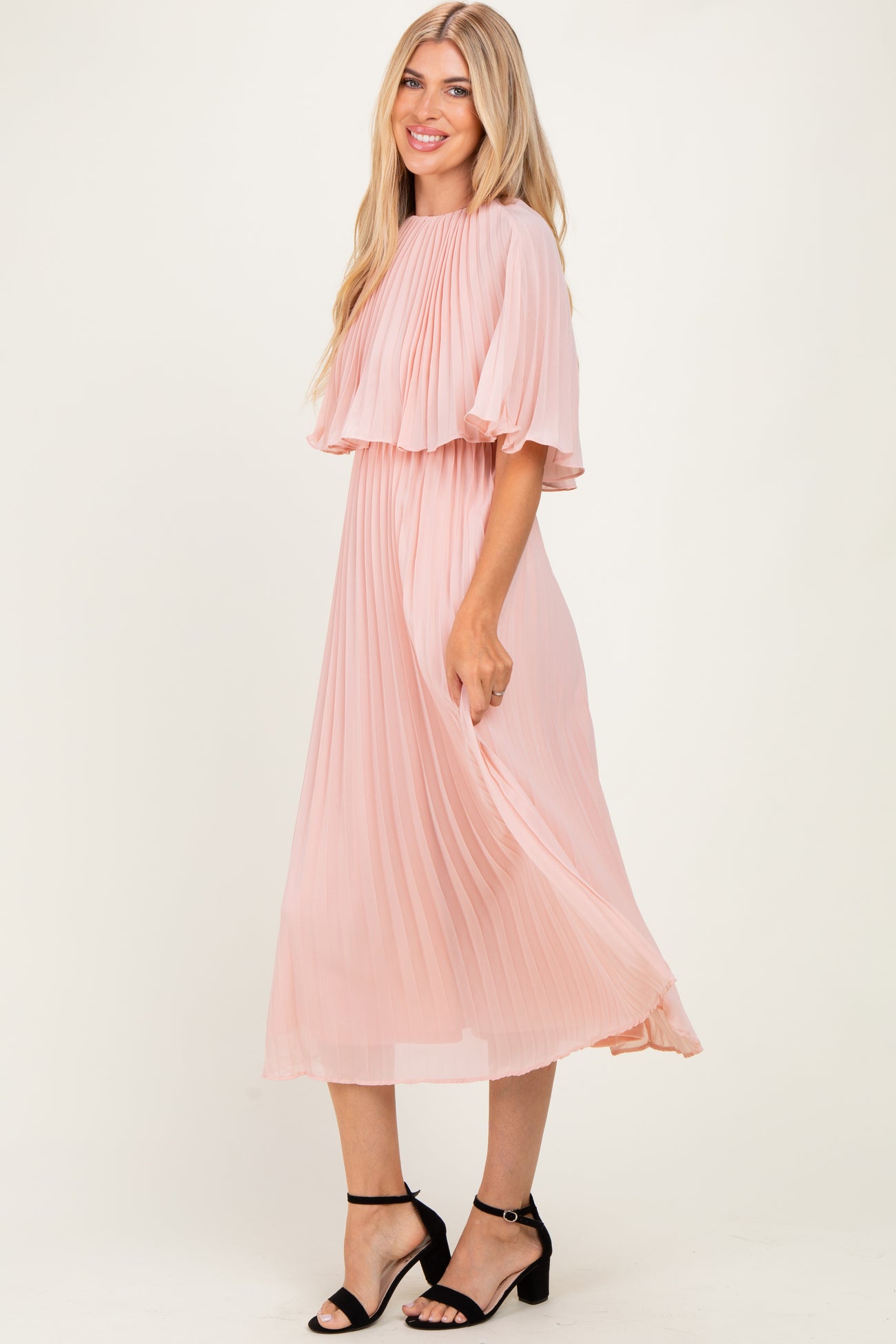 woman wearing a light pink pleated midi dress with flutter sleeves and a flowy silhouette
