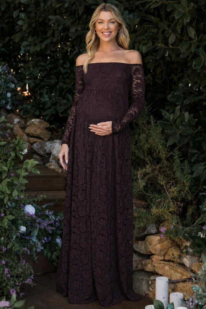 woman wearing a dark purple off-the-shoulder lace maternity dress and holding her baby bump in a garden setting