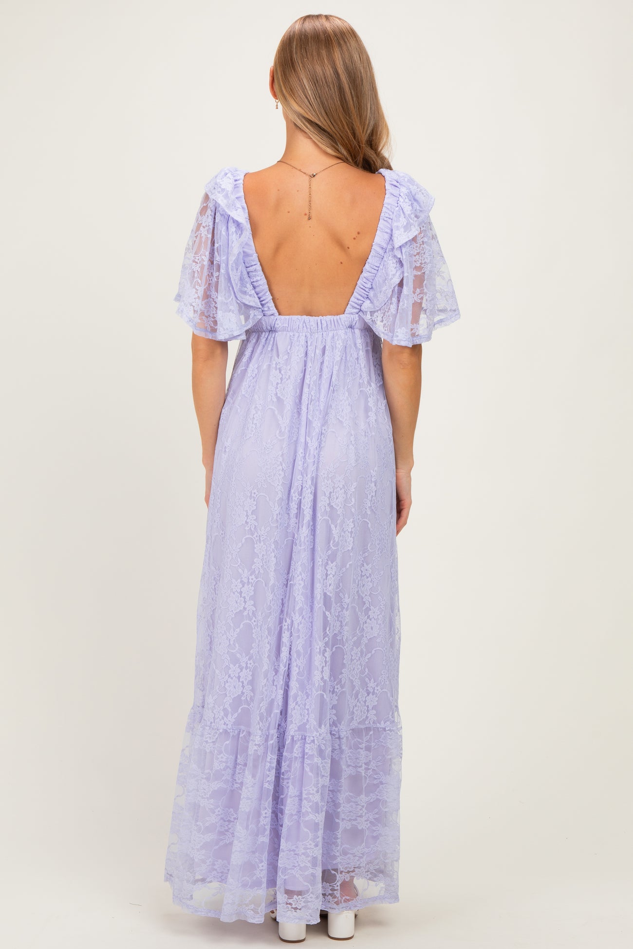 woman wearing a lavender long maxi dress with lace details and ruffled sleeves, showing an open back