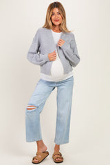woman wearing a gray cropped cardigan over a white top and blue ripped maternity jeans, showcasing her baby bump