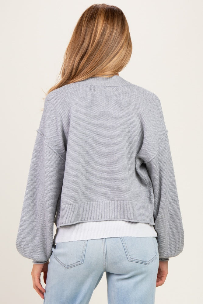 woman wearing a light gray cropped maternity cardigan with balloon sleeves, from the back
