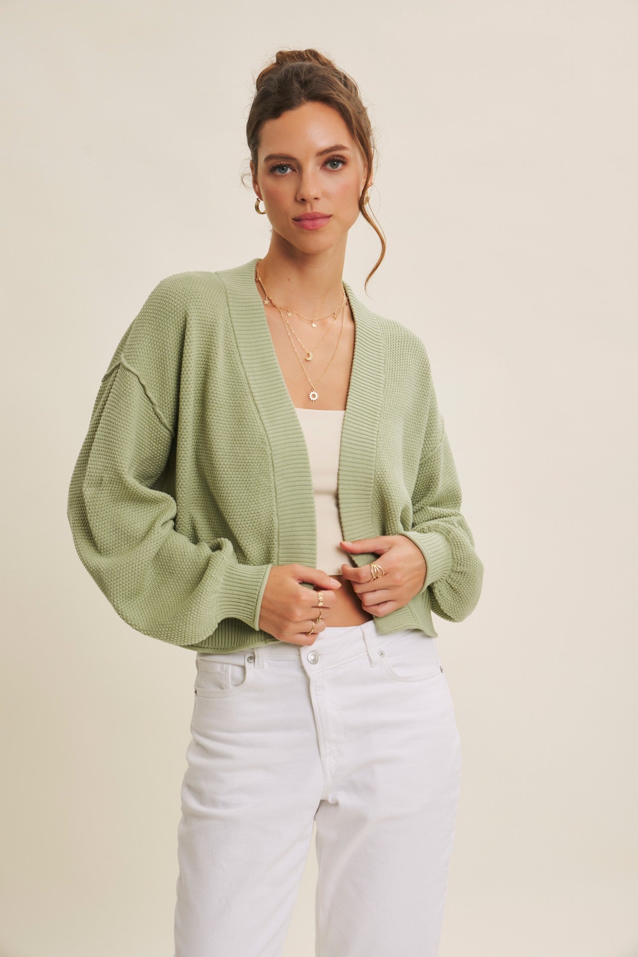 woman wearing a light green cropped cardigan over a beige tank top and white high-waisted jeans
