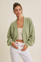 woman wearing a light green cardigan over a beige crop top and white high-waisted jeans