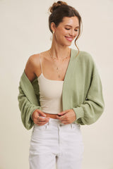 woman wearing a light green oversized cardigan over a beige tank top and white high-waisted jeans